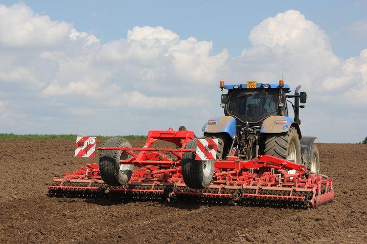 Niebieski ciągnik z maszyną rolniczą podczas prac polowych